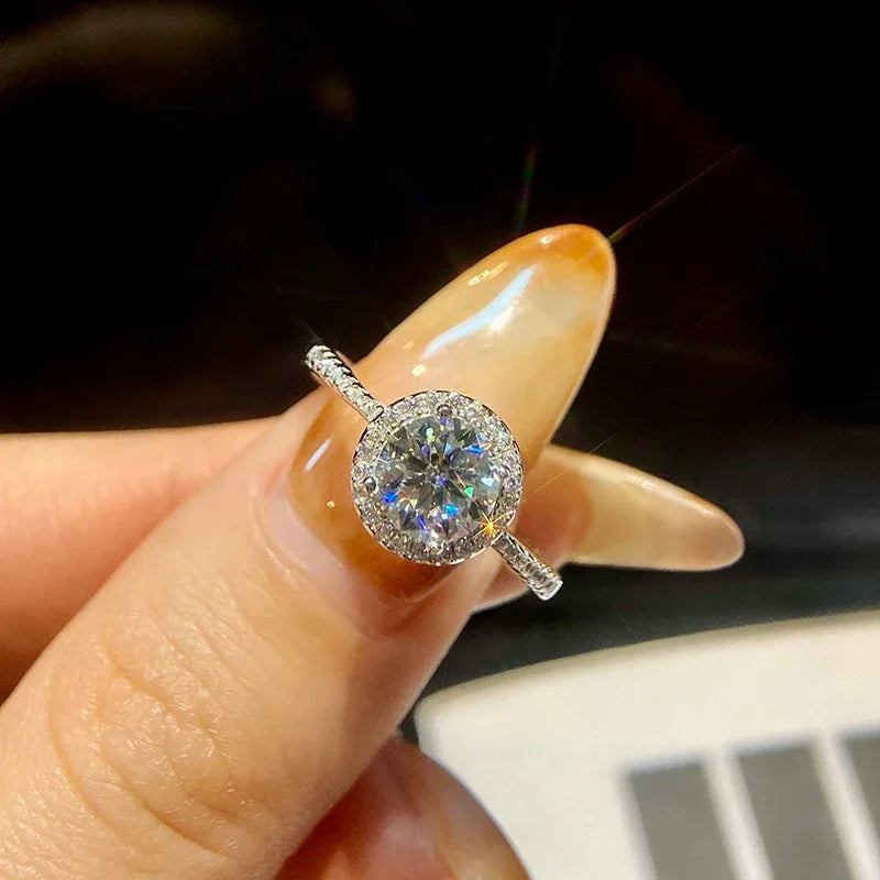 Silver ring with a diamond held between fingers against a dark background