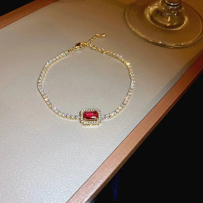 Gold bracelet with a red gemstone on a light surface