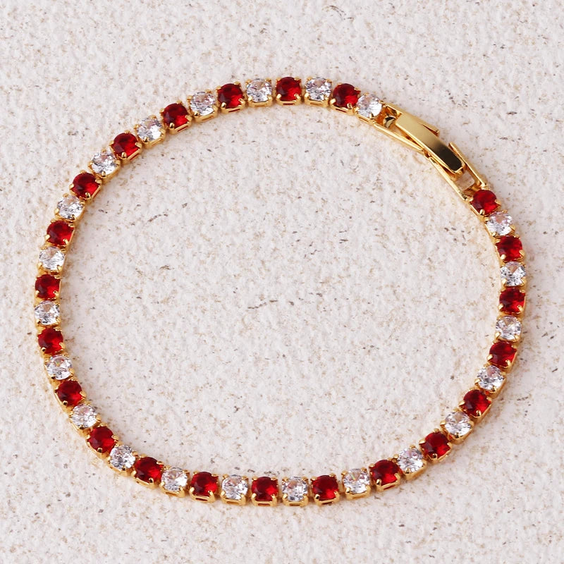 Gold bracelet with red and clear gemstones on a beige surface