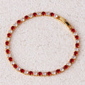 Gold bracelet with red and clear gemstones on a beige surface