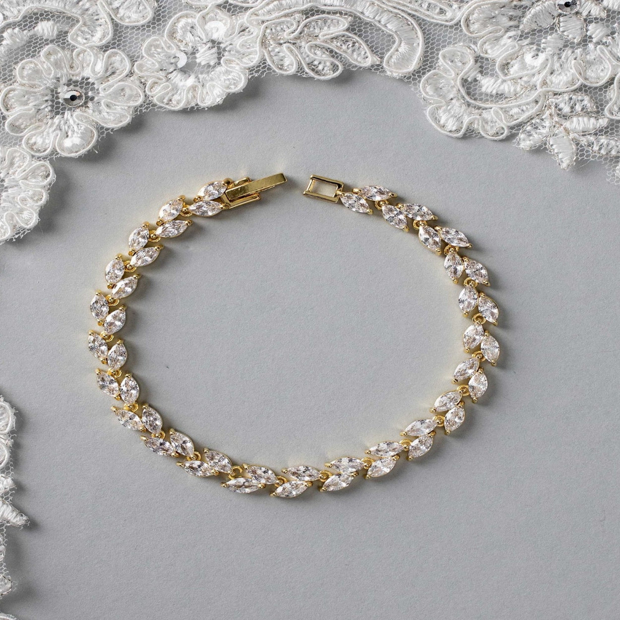 Gold and crystal bracelet on a gray surface with lace in the background