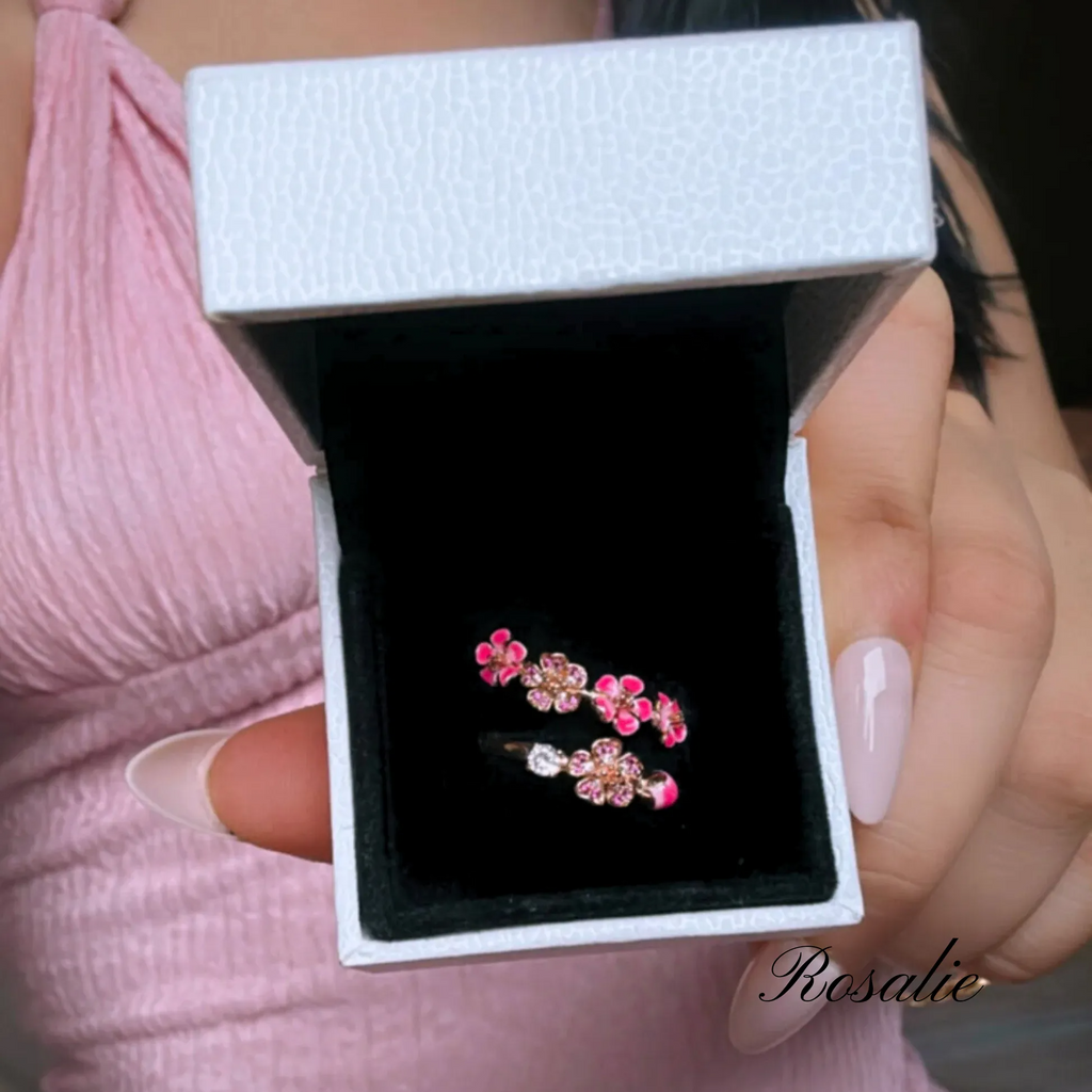 Pink floral earrings in a jewelry box held by a person with pink nail polish.