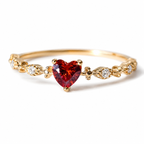 Gold ring with a heart-shaped red gemstone on a white background