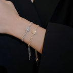 Two bracelets, one silver and one gold, on a person's wrist against a black background.