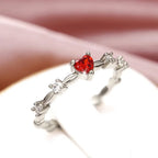 Silver ring with a red heart-shaped gemstone on a soft pink background