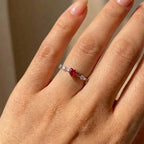 Hand wearing a ring with a red gemstone on a neutral background