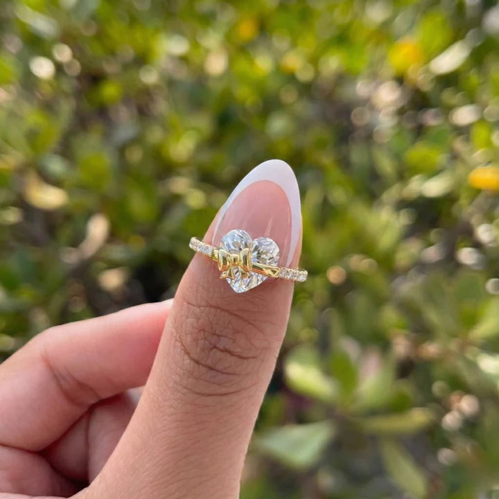 Gold ring with a diamond held on a finger against a blurred green background