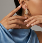 Close-up of a woman wearing a gold earring with a pearl-like finish, against a neutral background.